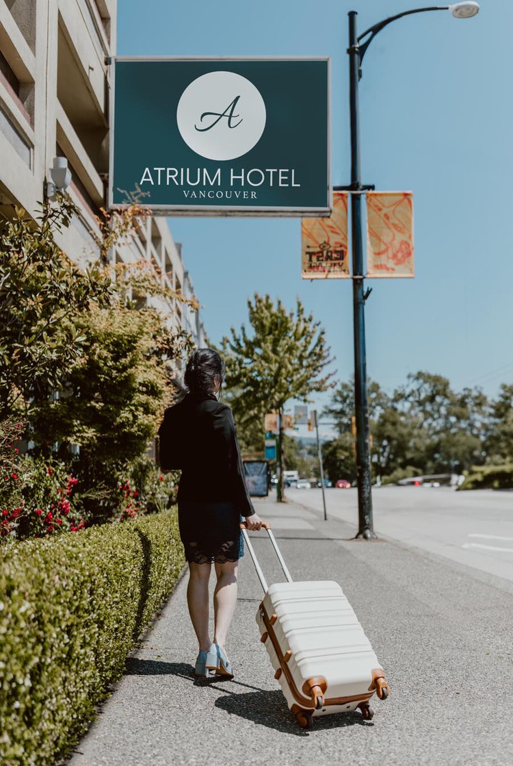 Woman standing with suitcase next to Atrium Hotel Vancouver sign